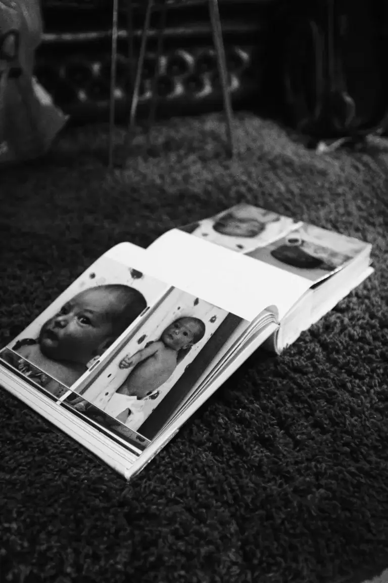 A baby photo album open on a carpeted floor, showing close-up images of a newborn child