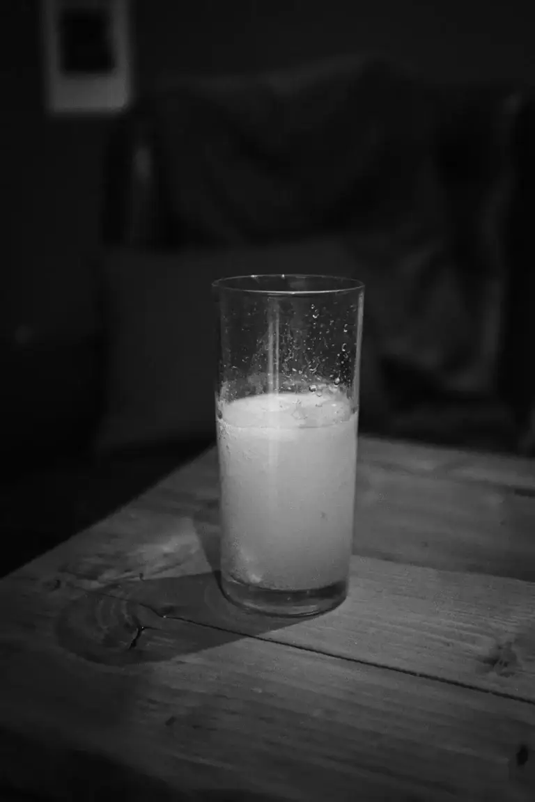 Black and white image of a cloudy half-full glass on a wooden table with condensation clinging to the sides