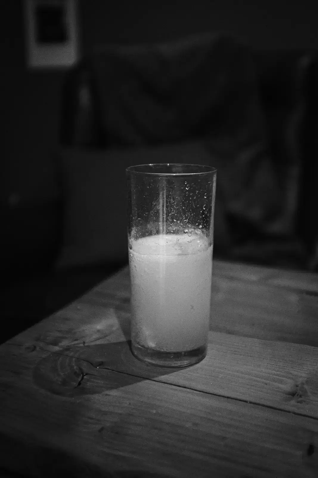 Black and white image of a cloudy half-full glass on a wooden table with condensation clinging to the sides
