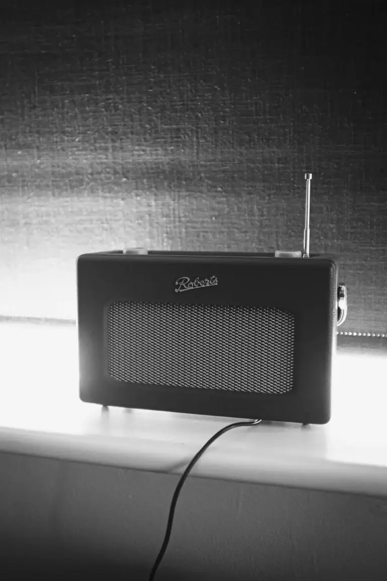 Black and white photo of a Roberts radio on a windowsill with a cable plugged in, softly lit from behind