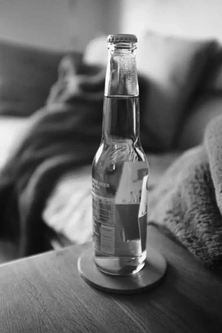 Black and white image of a sealed glass beer bottle on a wooden table in a domestic setting