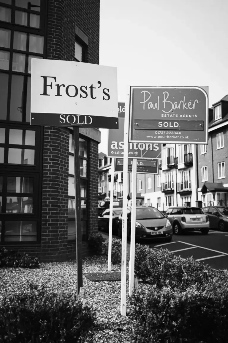 Black and white photo of multiple estate agent 'Sold' signs outside modern flats on a residential street