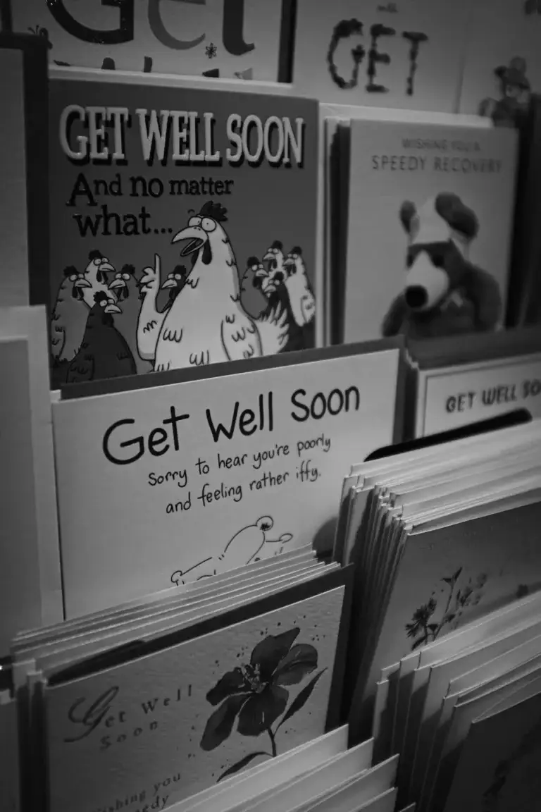 Black and white photo of a shop display filled with humorous and heartfelt 'Get Well Soon' cards