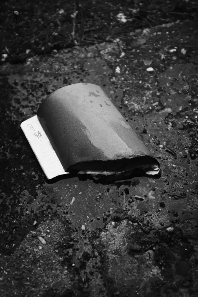 Black and white photo of a wet, half-buried notebook on a gritty pavement
