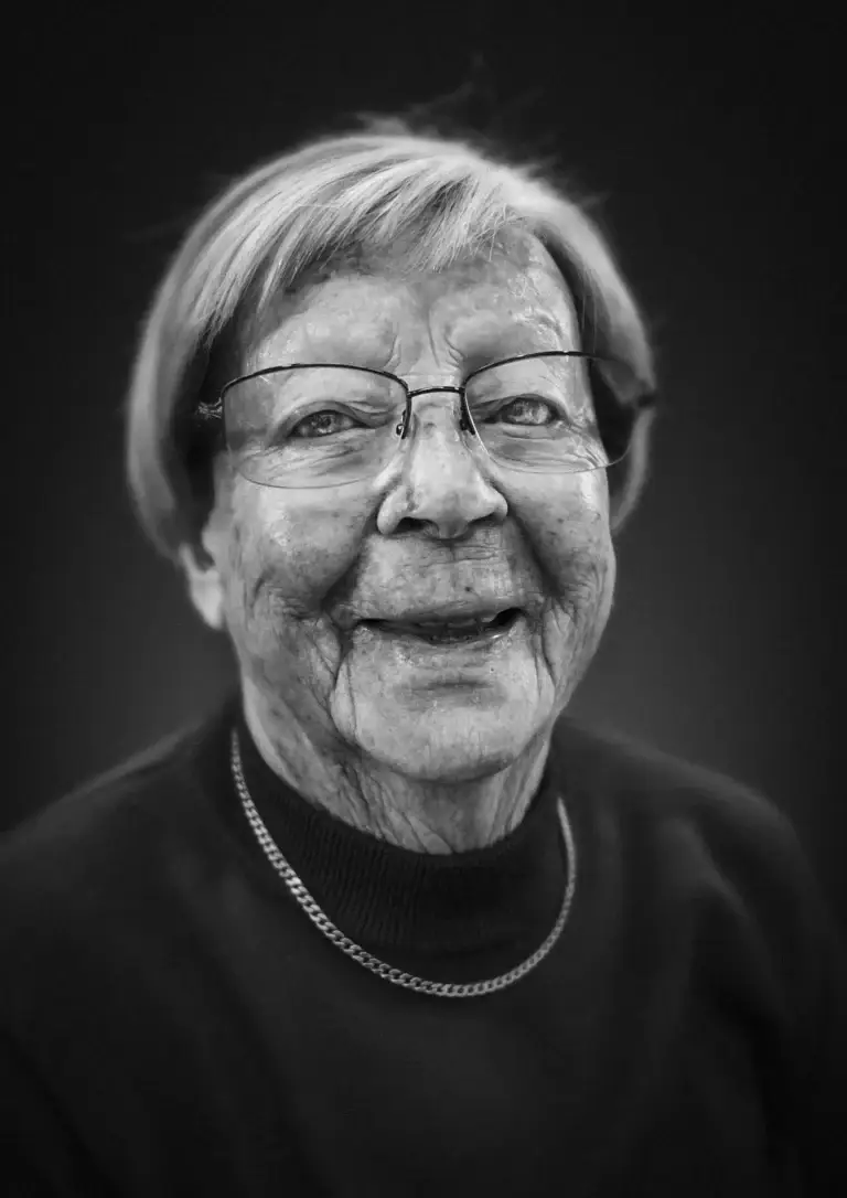 lack and white portrait of an elderly woman with short hair and glasses, smiling warmly at the camera