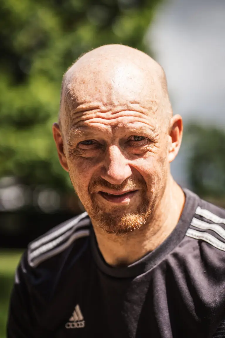 Bald man with a ginger goatee wearing a black Adidas shirt, looking directly into the camera under strong sunlight
