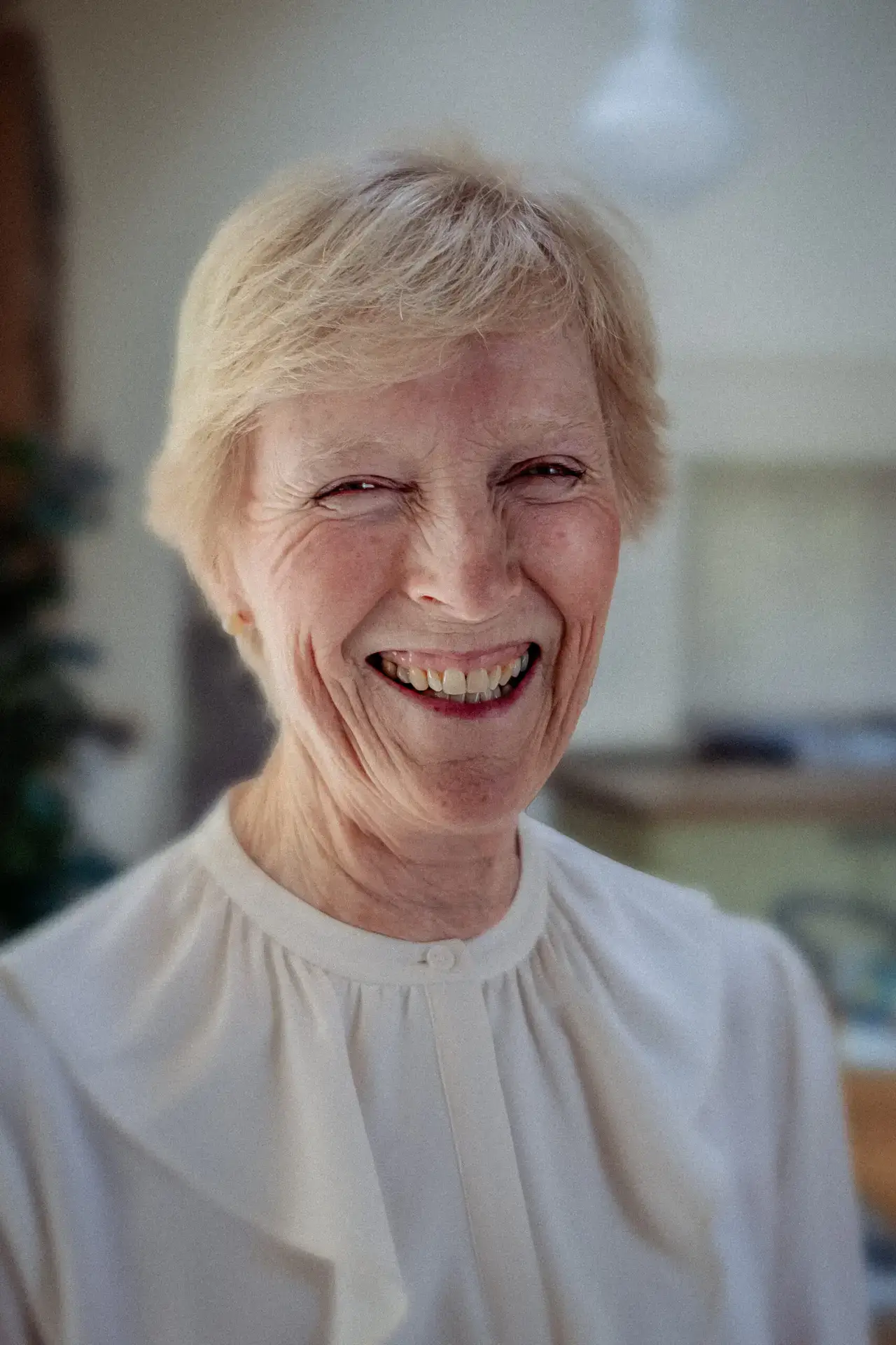 Portrait of Countess Howe smiling warmly, wearing a white blouse, with soft natural light and a neutral background.