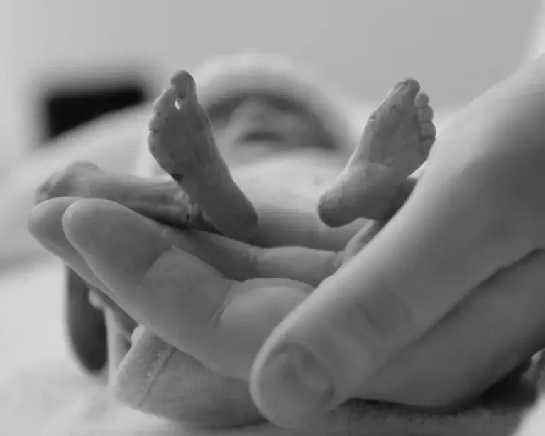 Black and white photo of a premature baby's tiny feet cradled gently in an adult's hand