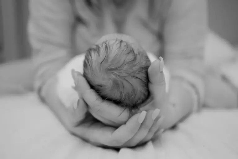 Black and white image of a woman gently cupping the back of a newborn baby’s head in her hands