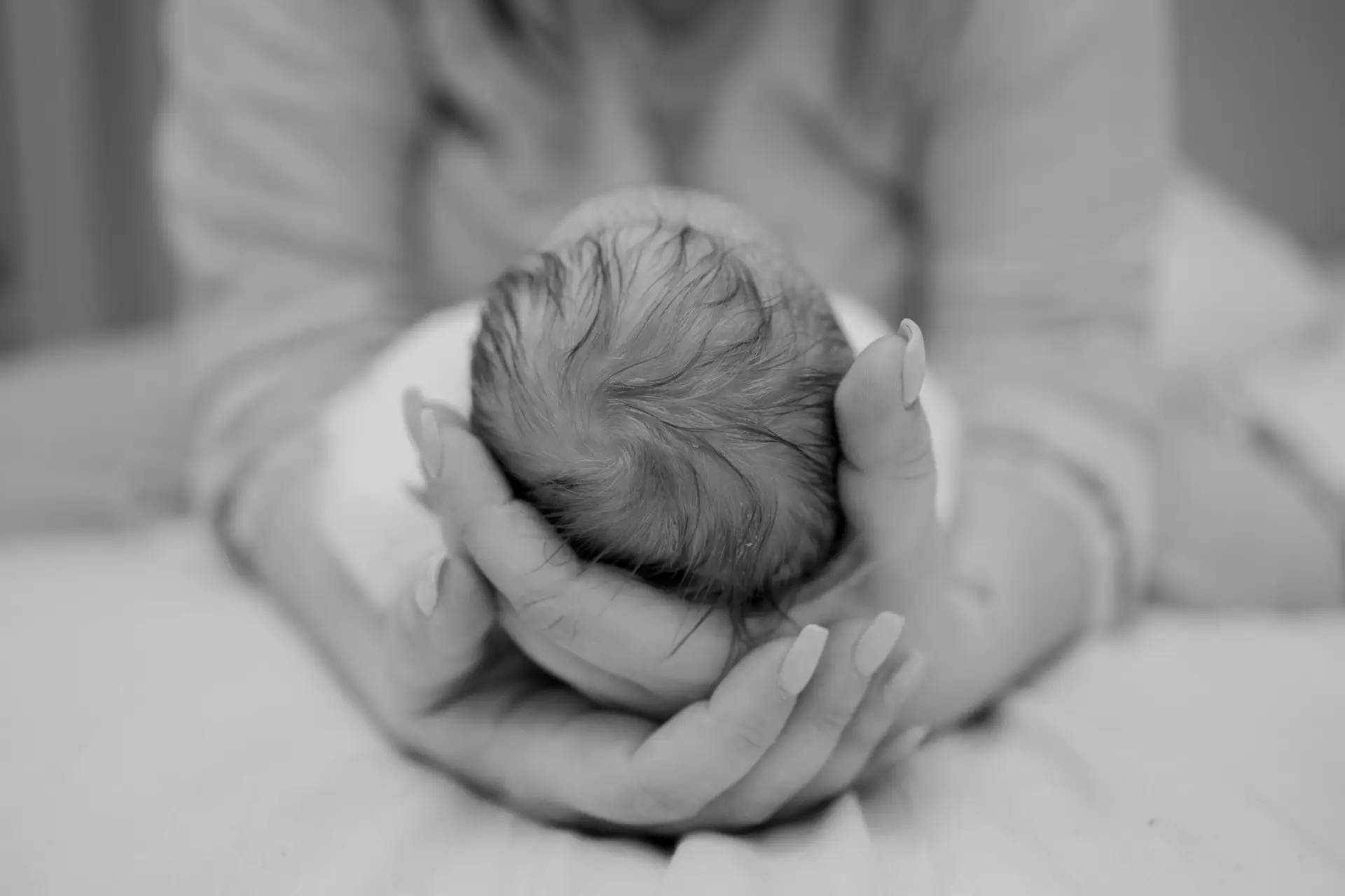Black and white image of a woman gently cupping the back of a newborn baby’s head in her hands