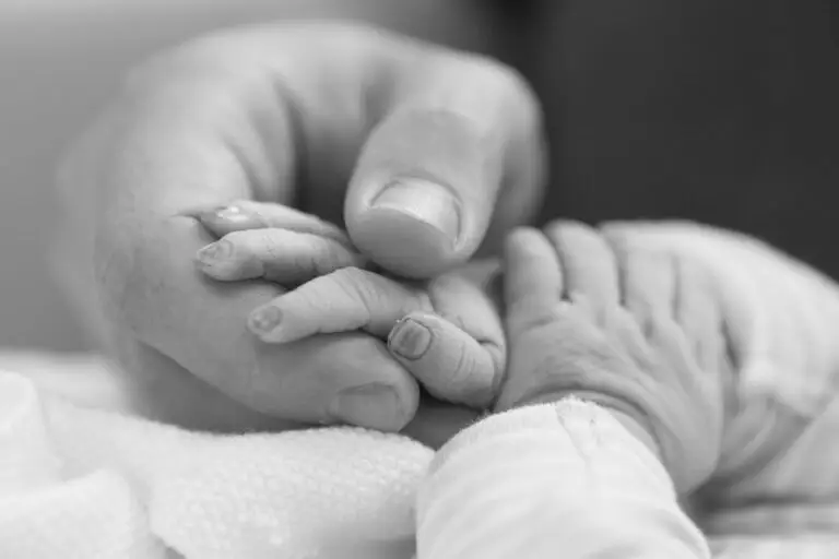 Black and white close-up of a newborn baby’s fingers gently wrapped around an adult’s thumb