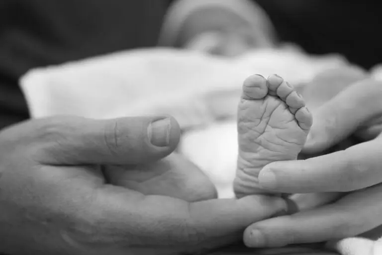 Black and white image of a newborn baby’s foot held gently between two adult hands
