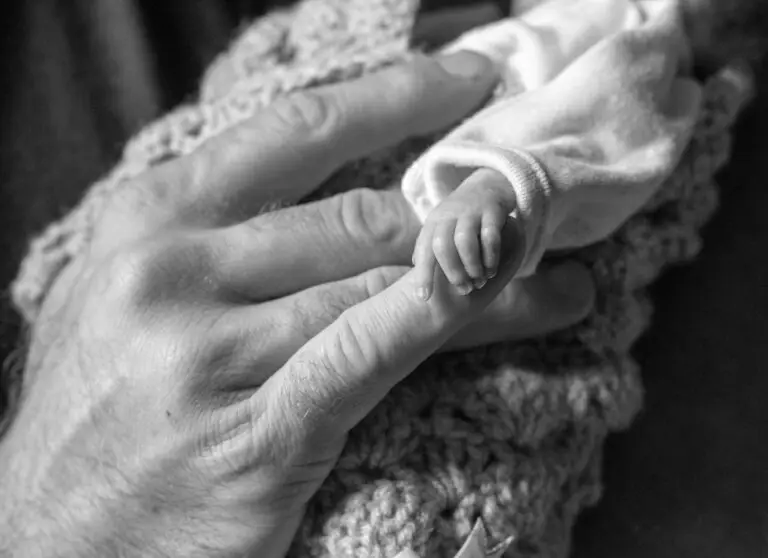 Black and white image of a newborn baby’s hand gently gripping an adult’s finger