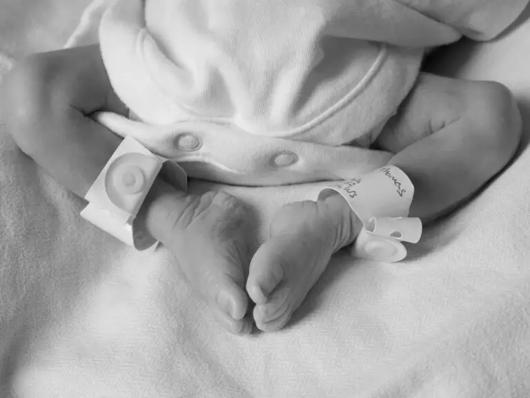 Black and white image of a newborn baby’s crossed feet with hospital ID bands reading “Thomas”