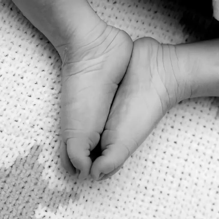 Black and white image of a baby’s feet resting gently together on a knitted blanket