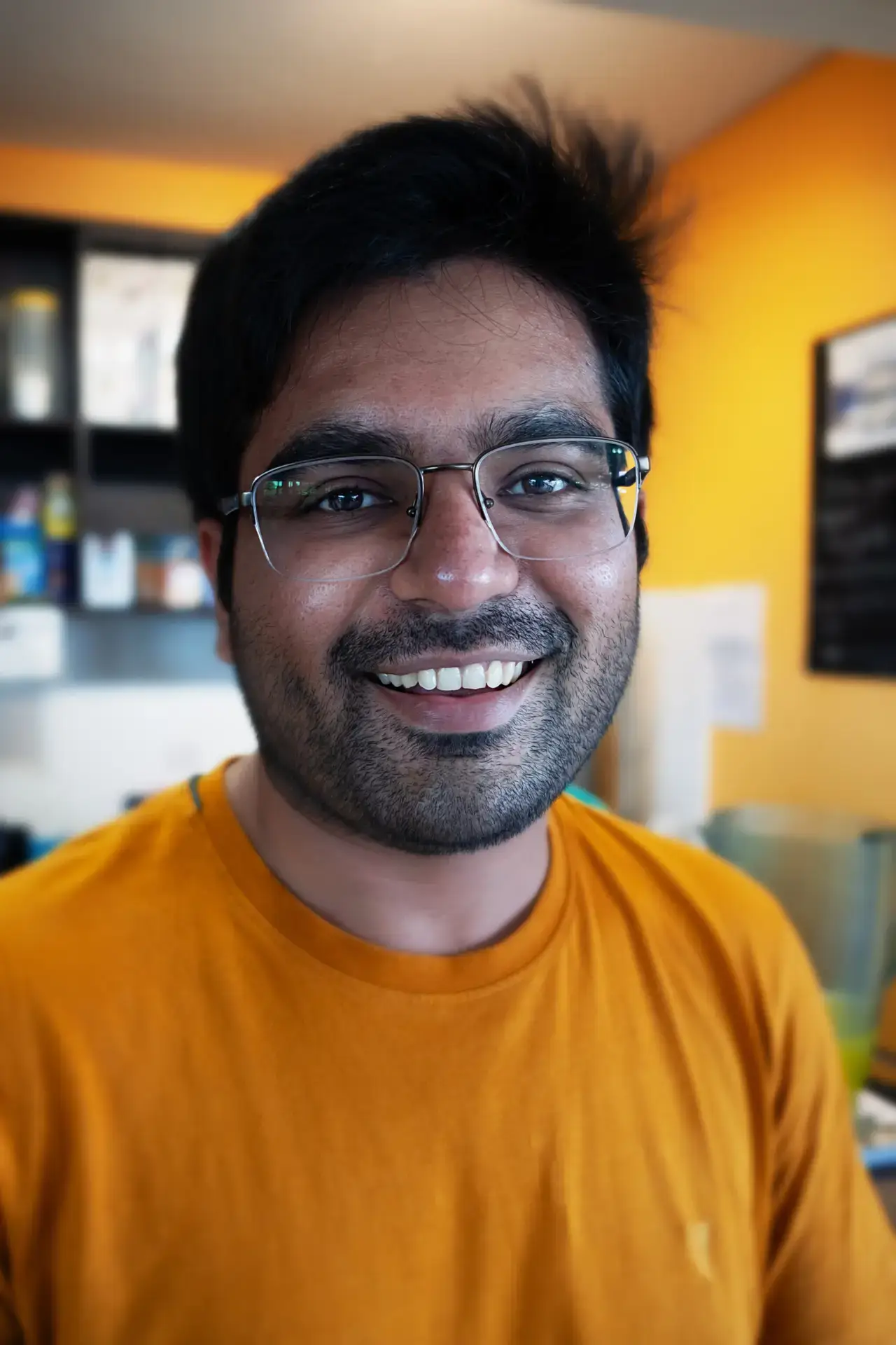 Smiling man in glasses wearing an orange shirt indoors.