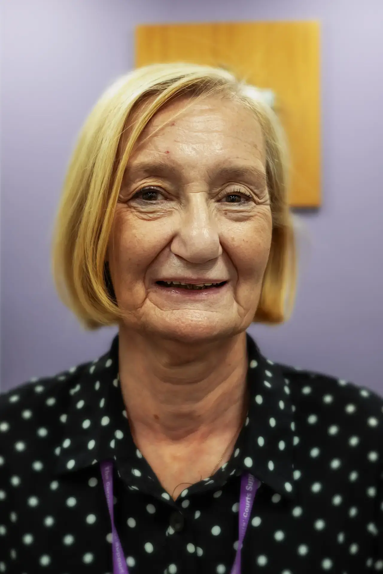 Woman with blonde hair wearing a polka dot shirt and purple lanyard.