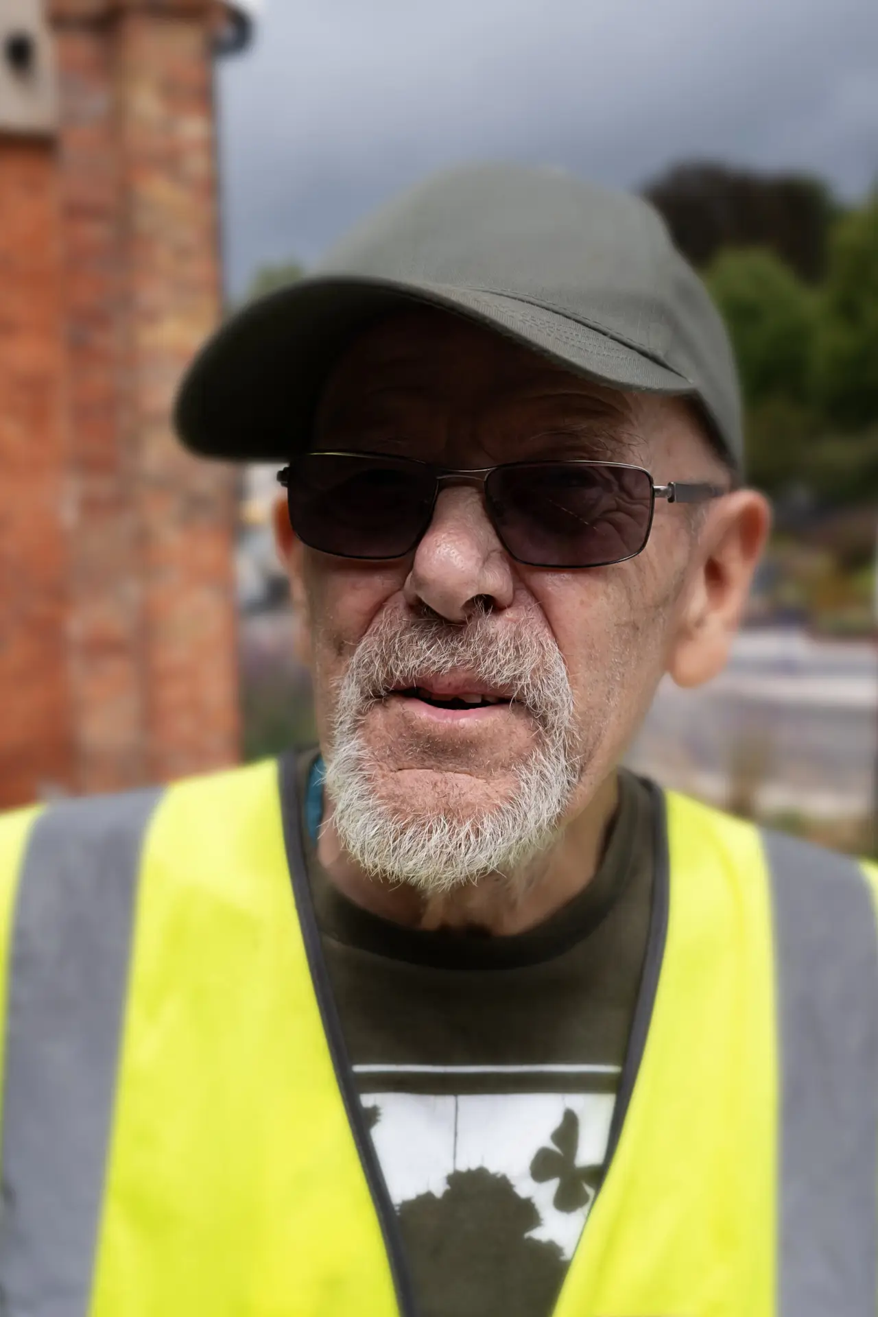 Older man in cap and sunglasses wearing a high-visibility vest outdoors