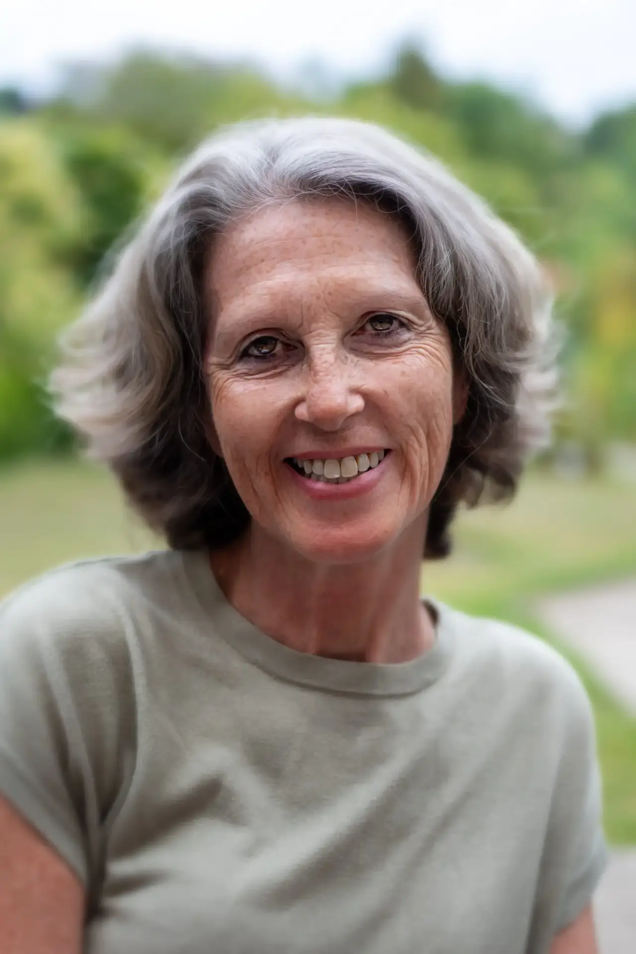Older woman with grey hair smiling outdoors in a green T-shirt.