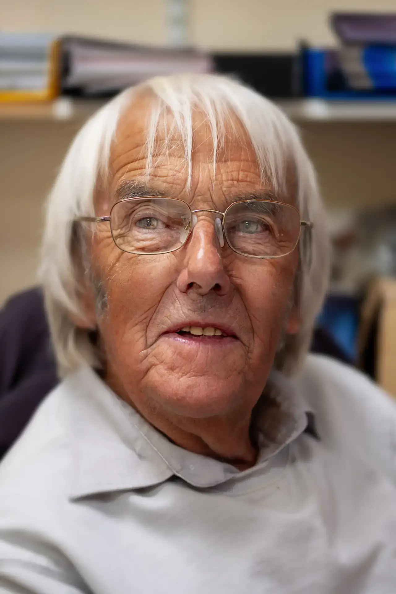 Older man with white hair and glasses wearing a light shirt indoors
