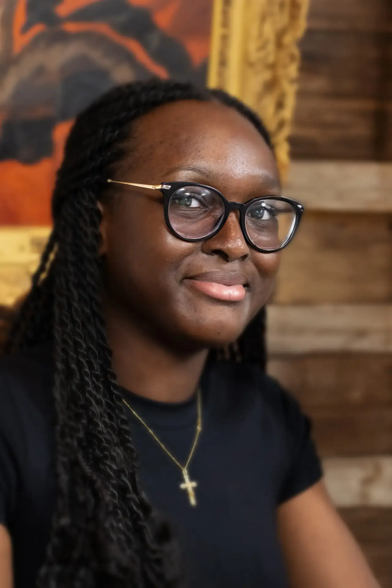Young woman with braided hair and glasses wearing a cross necklace and black top