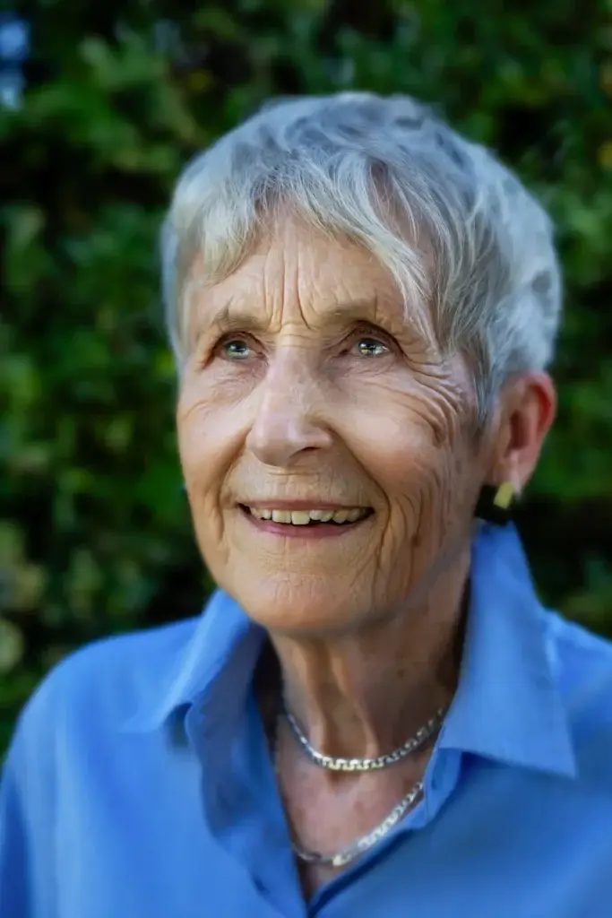 Smiling older woman with short grey hair wearing a blue shirt and necklace outdoors