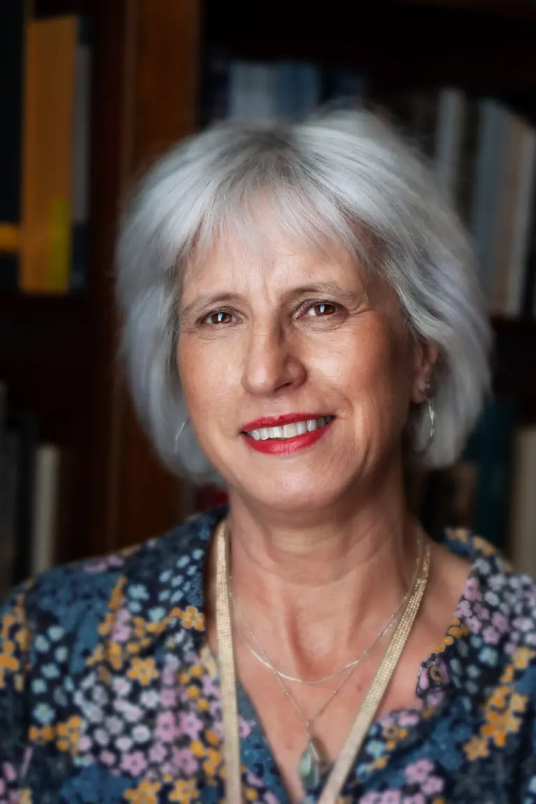 Smiling woman with short grey hair wearing a floral blouse and necklace indoors