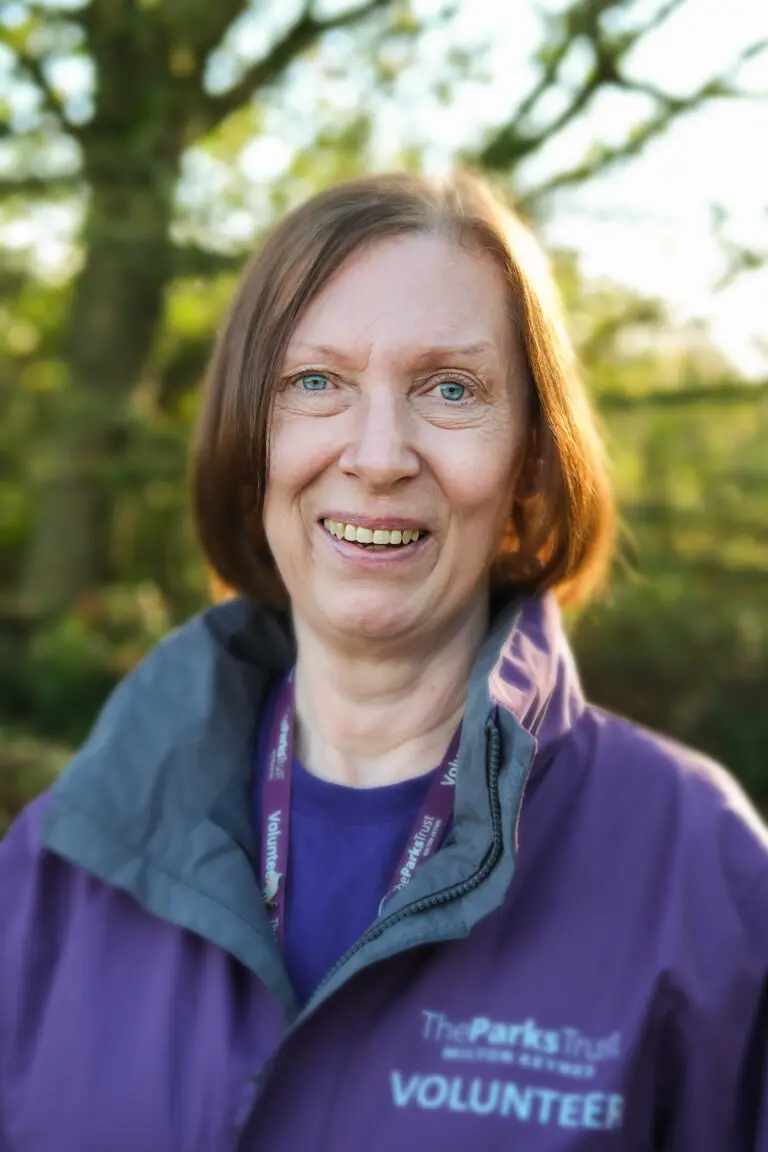 Smiling woman wearing a purple Parks Trust volunteer jacket standing outdoors