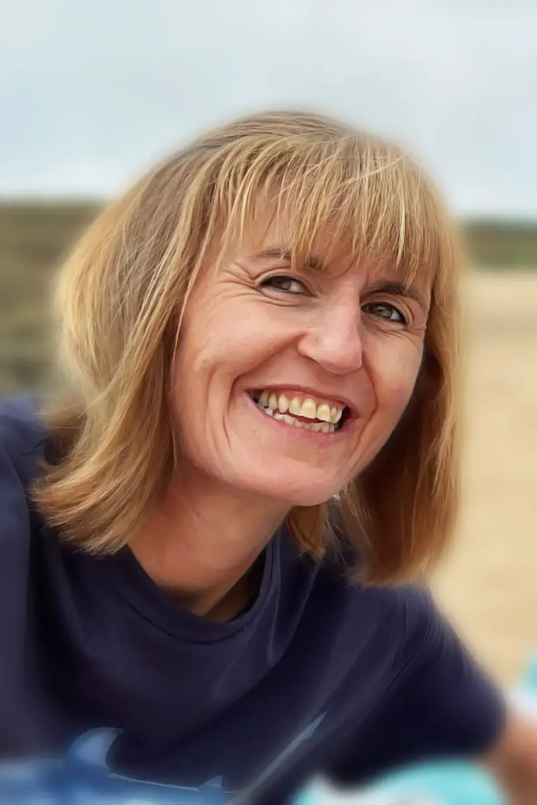 Smiling woman with blonde hair wearing a navy T-shirt outdoors on a beach