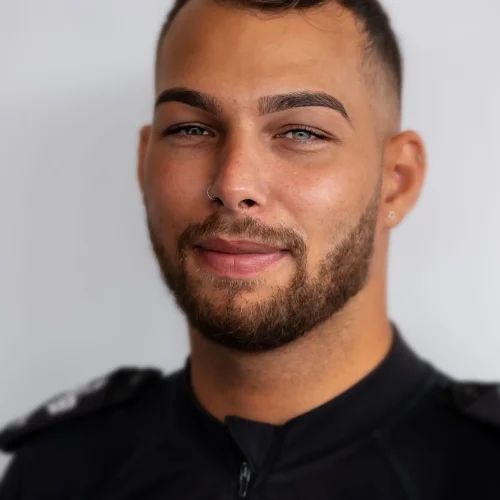 Smiling young man with beard, nose ring, and short hair wearing a dark uniform
