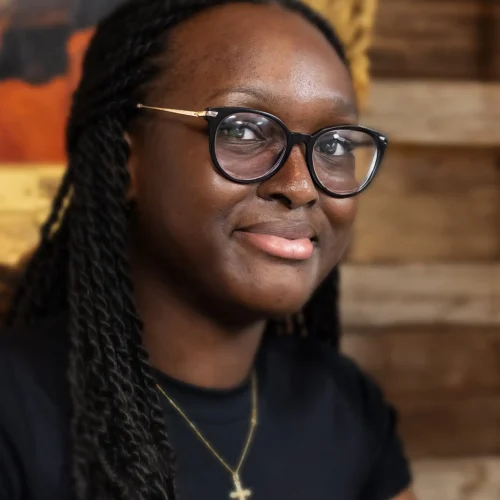 Young woman with braided hair and glasses wearing a cross necklace and black top