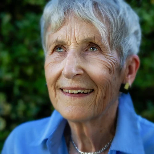 Smiling older woman with short grey hair wearing a blue shirt and necklace outdoors