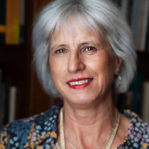 Smiling woman with short grey hair wearing a floral blouse and necklace indoors