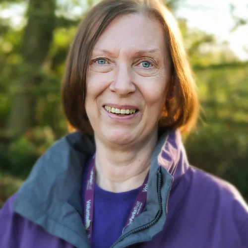Smiling woman wearing a purple Parks Trust volunteer jacket standing outdoors