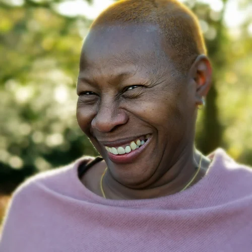 Smiling woman with short hair wearing a pink top outdoors in soft sunlight