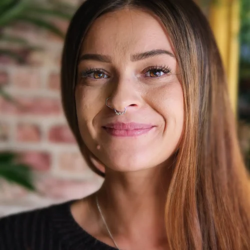Smiling woman with long straight hair and a nose ring in soft indoor lighting