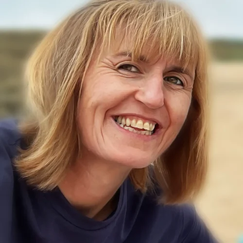 Smiling woman with blonde hair wearing a navy T-shirt outdoors on a beach